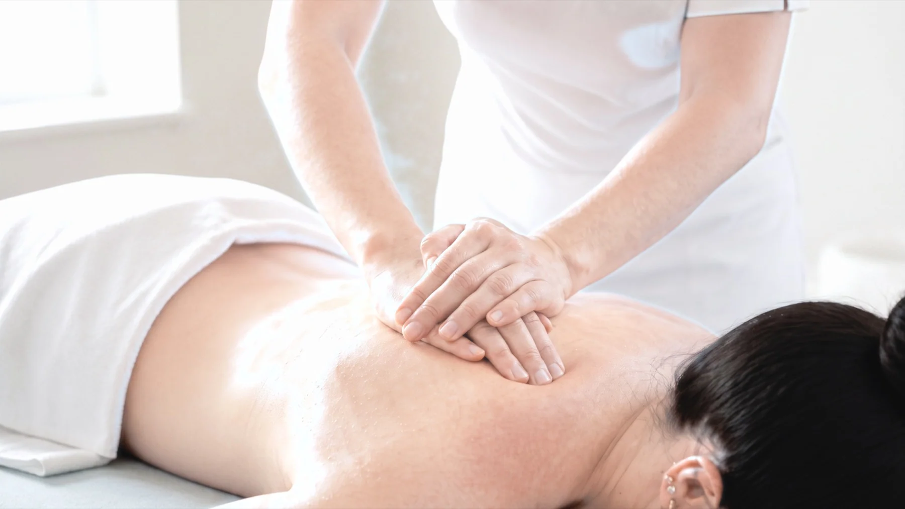 A therapist applying controlled, professional pressure across a client's upper back in a natural home setting. Avoid exaggerated force or expressions of pain.